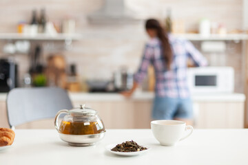 Woman preparing breakfast in kitchen and aromatic herbs for hot tea. Shot with background blur of lady having great morning with tasty natural healthy herbal tea sitting in the kitchen.
