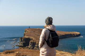 A young woman admires a beautiful view of the sea and rocks at Cape Tobizin on the Russky Island in...