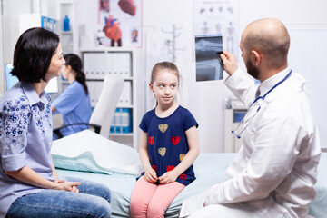 Obraz premium Friendly doctor holding x-ray during medical examination of child in hospital office. Healthcare physician specialist in medicine providing health care services treatment examination.