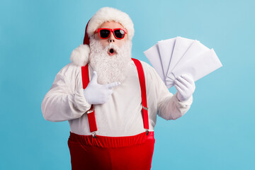 Fototapeta na wymiar Portrait of his he nice attractive amazed stunned thick white-haired Santa holding in hand demonstrating mail gifts wish list omg isolated bright vivid shine vibrant blue color background