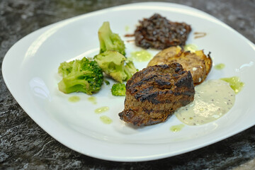meat, baked potatoes and cauliflower with sauce on a white plate