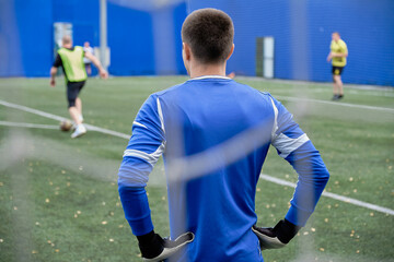 soccer goalkeeper in blue uniform at the gate looks at the players with the ball