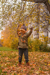 Little boy tossing leaves in autumn park. Orange, green colors.