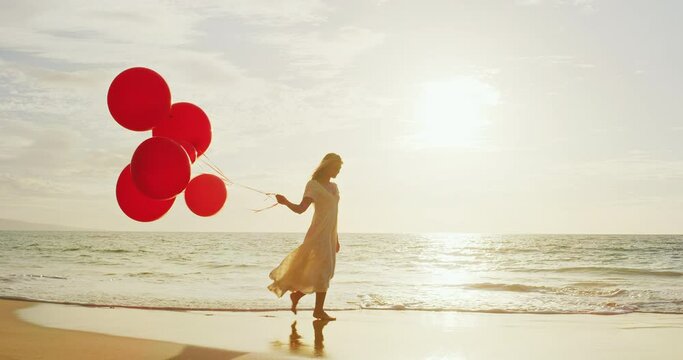 Beautiful happy young woman playing with red balloons on the beach
