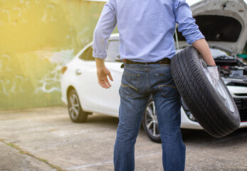 Obraz premium An Asian man is holding his spare tire ready to replace it after his car has a roadside puncture.