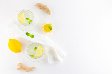 Ginger tea with lemon and mint on a white napkin. Two cups of ginger tea, lemon, ginger root and honey on white background. Top view