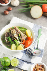 Sop Tulang Sapi or Indonesian clear  beef soup mixed with some vegetables such as carrot, potato, cabbage, and green bean. Served on ceramic bowl , with sambal and onion crackers as condiments.
