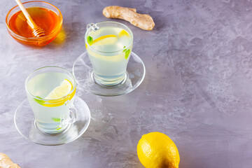 Obraz na płótnie Canvas Ginger tea with lemon on a gray background. Two cups of ginger tea and ingredients for its preparation. Copy space. Top view