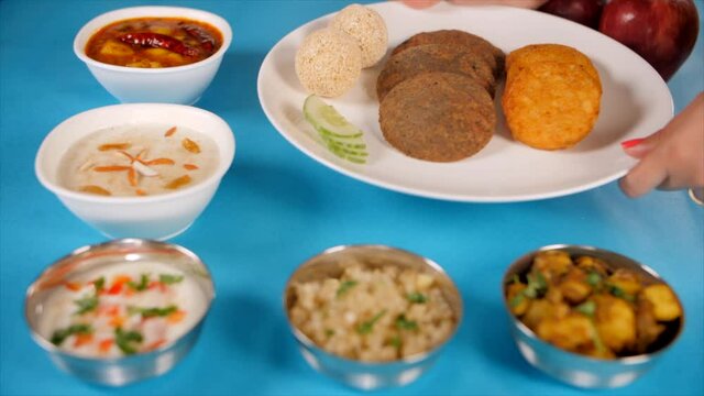 Hands of an Indian woman placing a thali of traditional Upwas/fasting food. Closeup shot of beautifully plated delicious Navratri food platter placed on a blue platform - Indian fasting concept