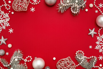 Christmas frame. White ornaments on red background, copy space. Pearl decor, fir twigs, flat lay.