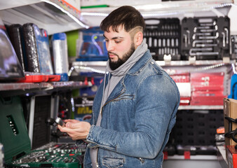 adult serious male is standing with new ratchet in tools store