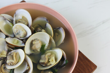 Kerang Kapah Rebus or boiled hard clam served on ceramic bowl on white marble background. Copy space.