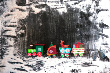 A toy wooden train carries gifts and Christmas paraphernalia on a dark, snow-covered background. Image for a decorative Christmas holiday concept. Winter frame. Free space for copying.