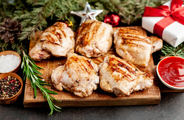 Christmas chicken thighs grilled without skin on a background of a stone with fir trees and fir toys, gifts