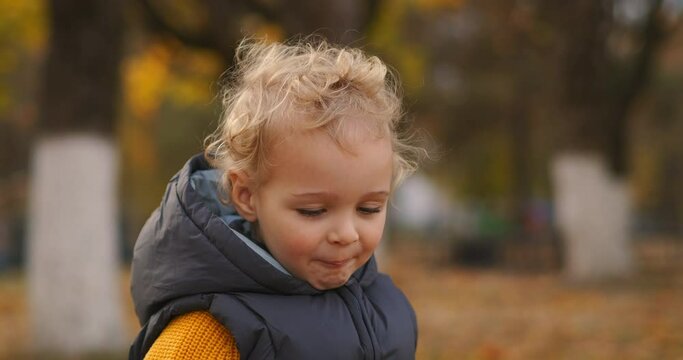 closeup portrait of little child with blonde curly hair in autumn park in city, funny face and grimacing of baby boy
