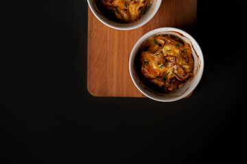 Mushroom julienne or mushroom casserole in two baking dish stands on a Board on a black background