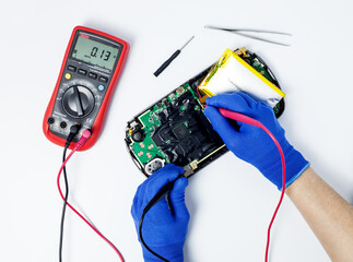 Hands of a person performing diagnostics with a multimeter of a portable game console on an...