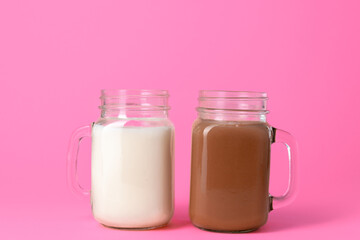 Glass jars with flavoured milkshakes against pink background