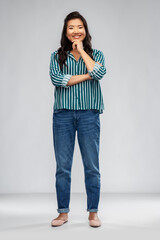 people, ethnicity and portrait concept - happy smiling asian young woman thinking over grey background