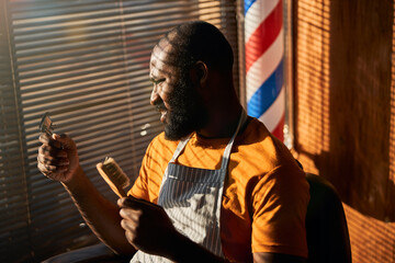 Handsome male barber holding hair trimmer and brush