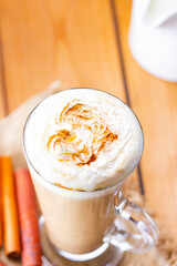 Pumpkin latte and milk jug on wooden boards. Pumpkin spice latte with whipped cream and piece of pumpkin. Hot autumn drink on a burlap