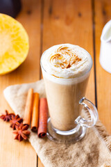 Pumpkin latte and milk jug on wooden boards. Pumpkin spice latte with whipped cream and piece of pumpkin. Hot autumn drink on a burlap