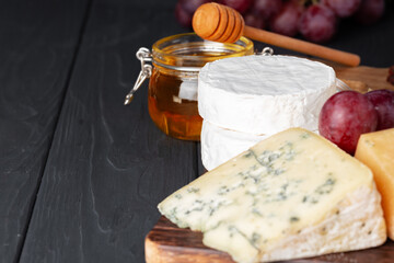Cheese served with grapes and honey on grey surface