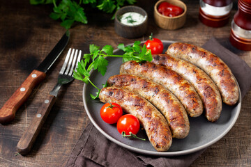 Fried sausages. Grilled sausages with spices, sauce, tomatoes and parsley. Delicious meat sausages in a ceramic plate