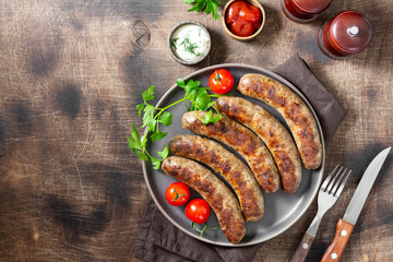 Fried sausages. Grilled sausages with spices, sauce, tomatoes and parsley. Delicious meat sausages in a ceramic plate. Top view with copyspace