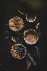 baking blueberry mini tarts dark moody wooden background top view