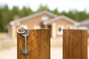 The key to the house is hanging on the fence. Background of cottage. Dream of home, building, design, delivery of the project, moving to new house, mortgage, rent and purchase real estate. Copy space