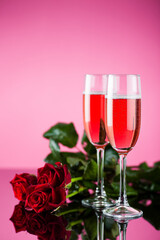 Studio photo of pink champagne with red roses on pink background and reflective surface.