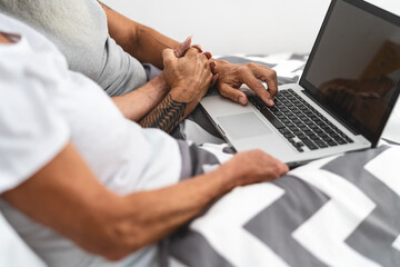 Senior couple using portable computer in bed - Mature people having fun with laptop while lying below blankets in bedroom - Elderly love relationship lifestyle and technology concept