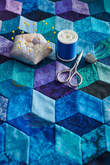 Pincushion, spool of thread, scissors and thimble on the tumbling blocks quilt background