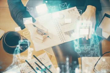 E-mail envelop theme hologram over hands taking notes background. Concept of electronic mail. Double exposure