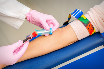 Nurse on pink gloves takes blood sample from vein from female patient in medical laboratory