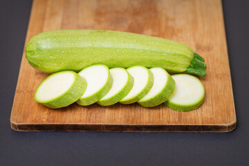 Slices of courgettes on wooden chopping board. Fresh green zucchini whole and cut into slices on cutting board
