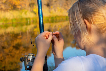 Young woman fisherman prepares to fish. Puts live bait (worm) on the hook of fishing rod with...