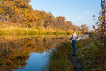 Fototapeta na wymiar Fishing in autumn on the river. Young woman holds fishing rod above surface of water