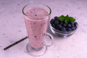 

Organic blueberry smoothie in a tall glass and fresh blueberries on a white background.