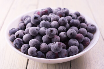 Frozen blueberries in a white plate on a white wooden background.