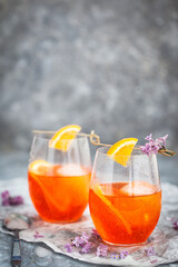 Orange Aperol Spritz cocktail served in a wine glasses, decorated with slice of orange and lilac