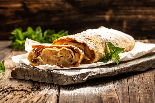 Traditional piece of apple strudel with powdered sugar and mint closeup on a wooden background. copy space