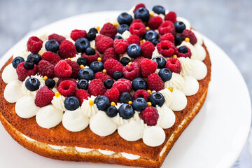 Delicious homemade heart shaped vanilla cake decorated with cream and fresh berries