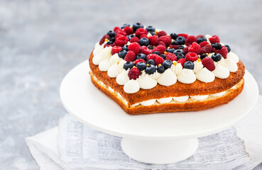 Delicious homemade heart shaped vanilla cake decorated with cream and fresh berries