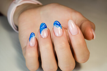 Hands of a young woman. The nails are covered with a light colored gel Polish with a bright design. Manicure ideas.