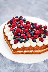 Delicious homemade heart shaped vanilla cake decorated with cream and fresh berries
