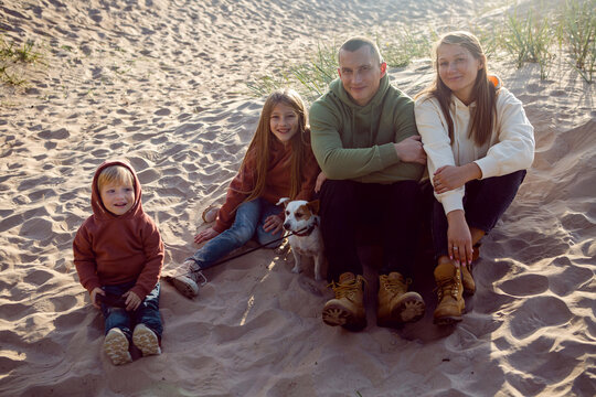 family with a son and daughter and a dog sit on the sand