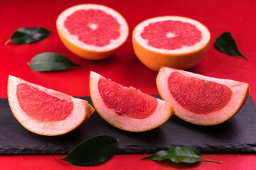 
Slices of grapefruit on a black slate board on a red background.
Close-up.