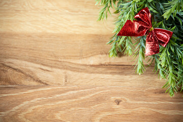 close-up of red, glossy bow and green wreath on wooden background, christmas decoration with shiny ribbon, flat lay